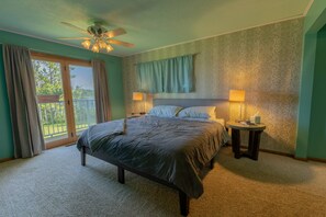 Ein Schlafzimmer mit einem Bett, zwei Nachttischlampen, einem Deckenventilator und Blick durch eine Schiebetür.