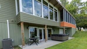 Ein zweigeschossiges Gebäude mit überdachter Terrasse, ausgestattet mit Tisch und Stühlen, einem Whirlpool und einem Mülleimer.
