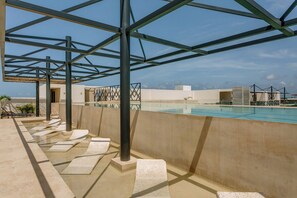 Ein Dachpool unter blauem Himmel, mit einer Pergola und Blick auf entfernte Gebäude.