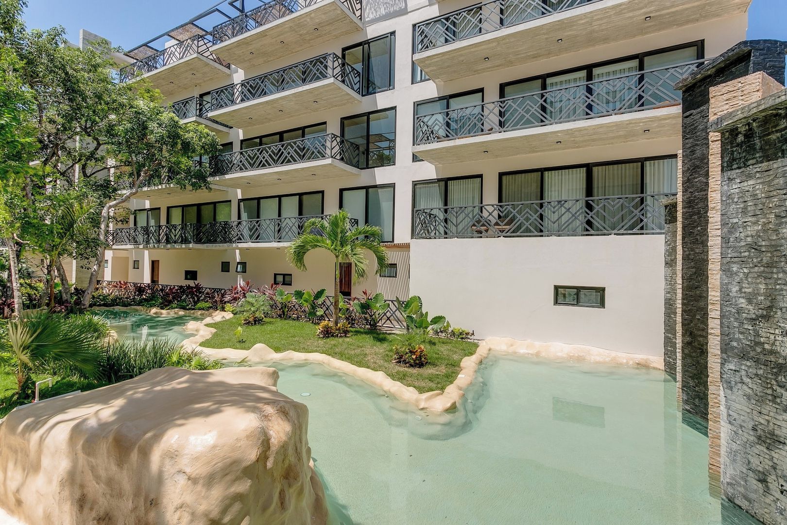A multi-story hotel with balconies, a swimming pool, and lush landscaping.