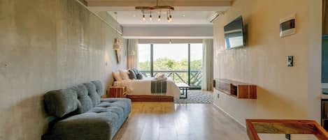 A modern bedroom with a large bed, a sofa, a TV, and a balcony with a view.