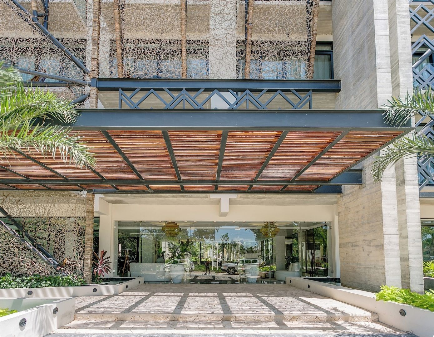 A hotel entrance with a covered walkway, glass doors, and a view of the surrounding greenery.