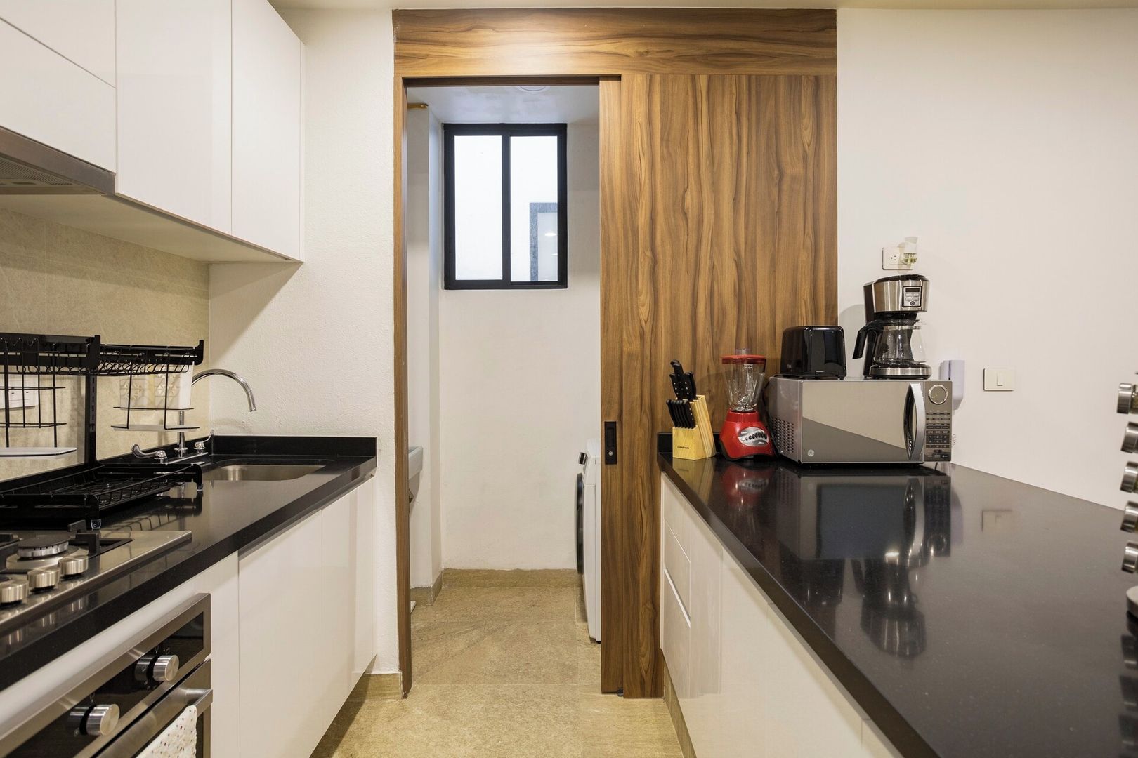 A modern kitchen with a black countertop, stainless steel appliances, and a wooden door leading to a hallway.