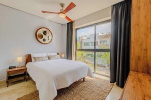 Un dormitori amb un llit gran, un ventilador de sostre, una decoració circular a la paret i vistes per una finestra ampla.