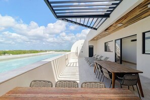 Una zona d'exterior enllocada per dinar amb piscina, una taula de fusta i seients de relax.