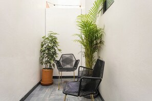 A small, enclosed outdoor area with a potted plant, two black chairs, and a tall plant against a white wall. - Please note: electricity is not included in reservations longer than 28... (Tulum)