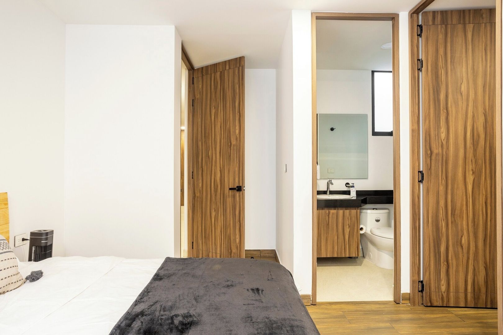 Un dormitorio con cama, mesita de noche, armario y baño visible a través de una puerta abierta.
