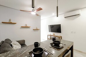 A modern living room with a dining area, a ceiling fan, a flat-screen TV, and minimalist decor. - Please note: electricity is not included in reservations longer than 28... (Tulum)