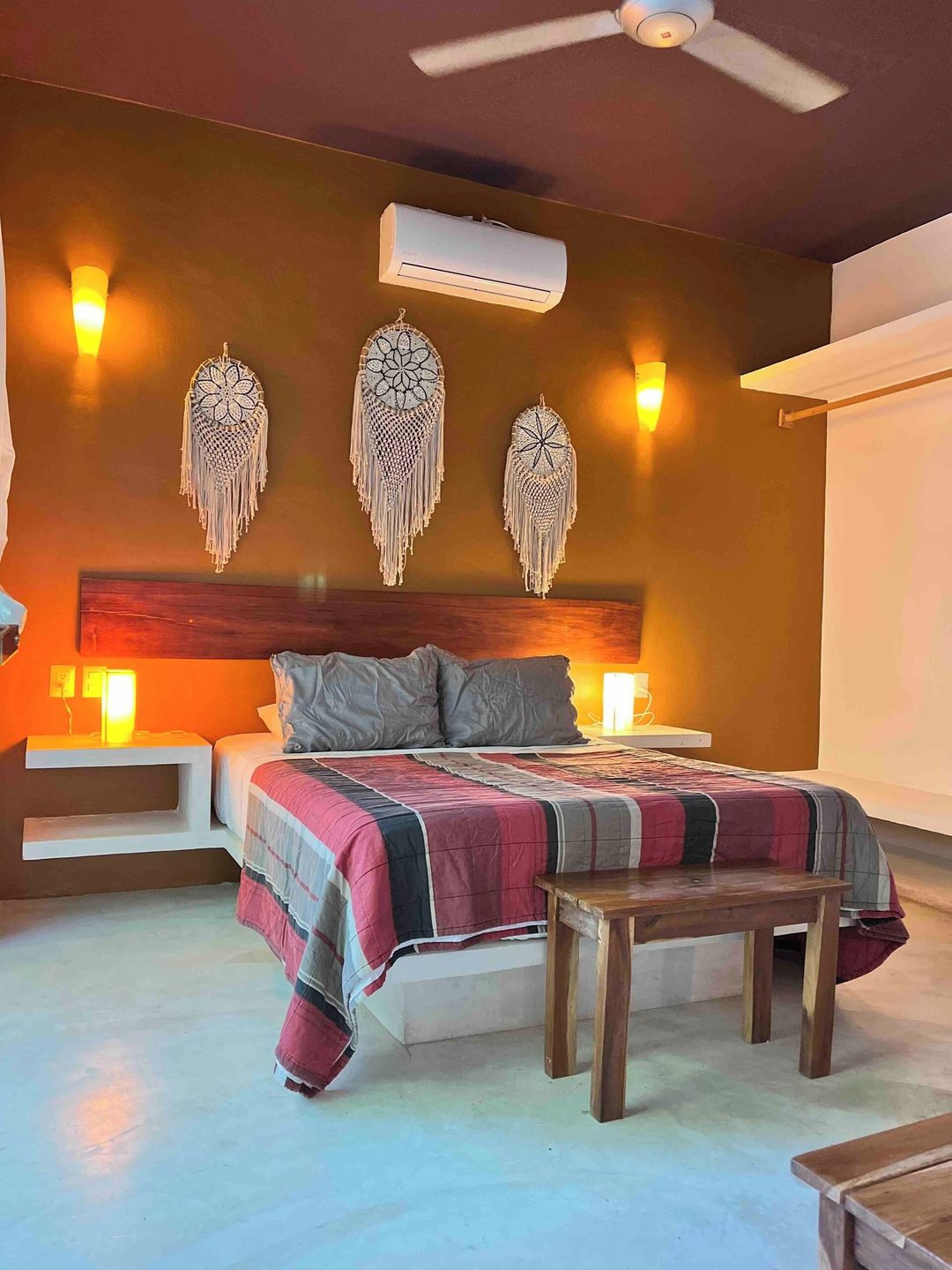 Un dormitorio con cama, mesitas de noche, aire acondicionado instalado en la pared, adornos decorativos en la pared y un ventilador de techo.