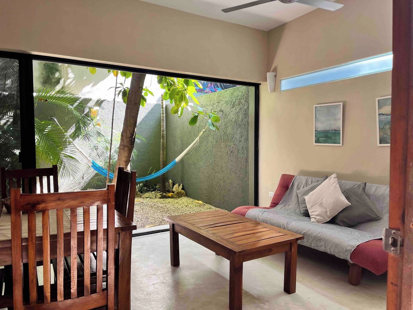 A room with a sliding glass door leading to a garden, a wooden bench, a sofa, and a small table.