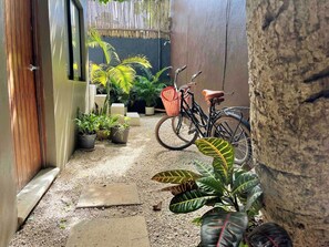 A narrow pathway leading to a wooden door, surrounded by potted plants and a bicycle. - Downtown Tulum Cozy 1bd Apartment (Tulum)