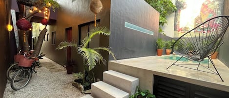 A modern outdoor space with a concrete bench, a bicycle, potted plants, and a tree with hanging lights.