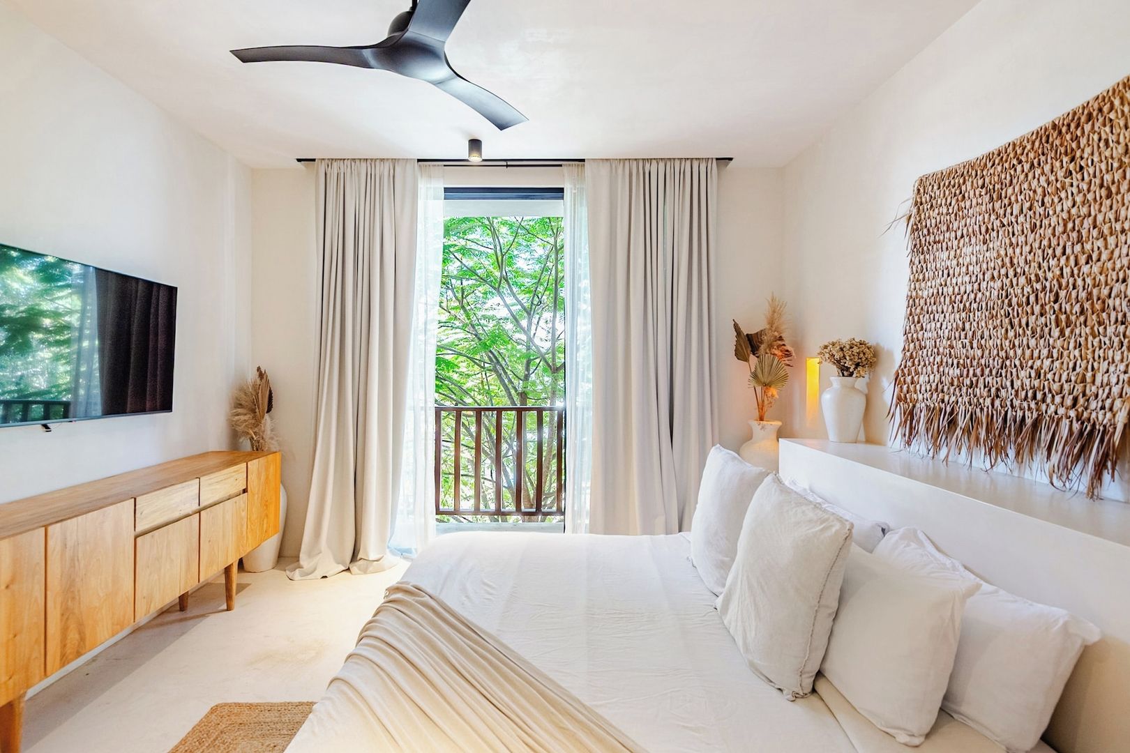 A modern bedroom with a bed, a TV, a wooden dresser, and a balcony with curtains.