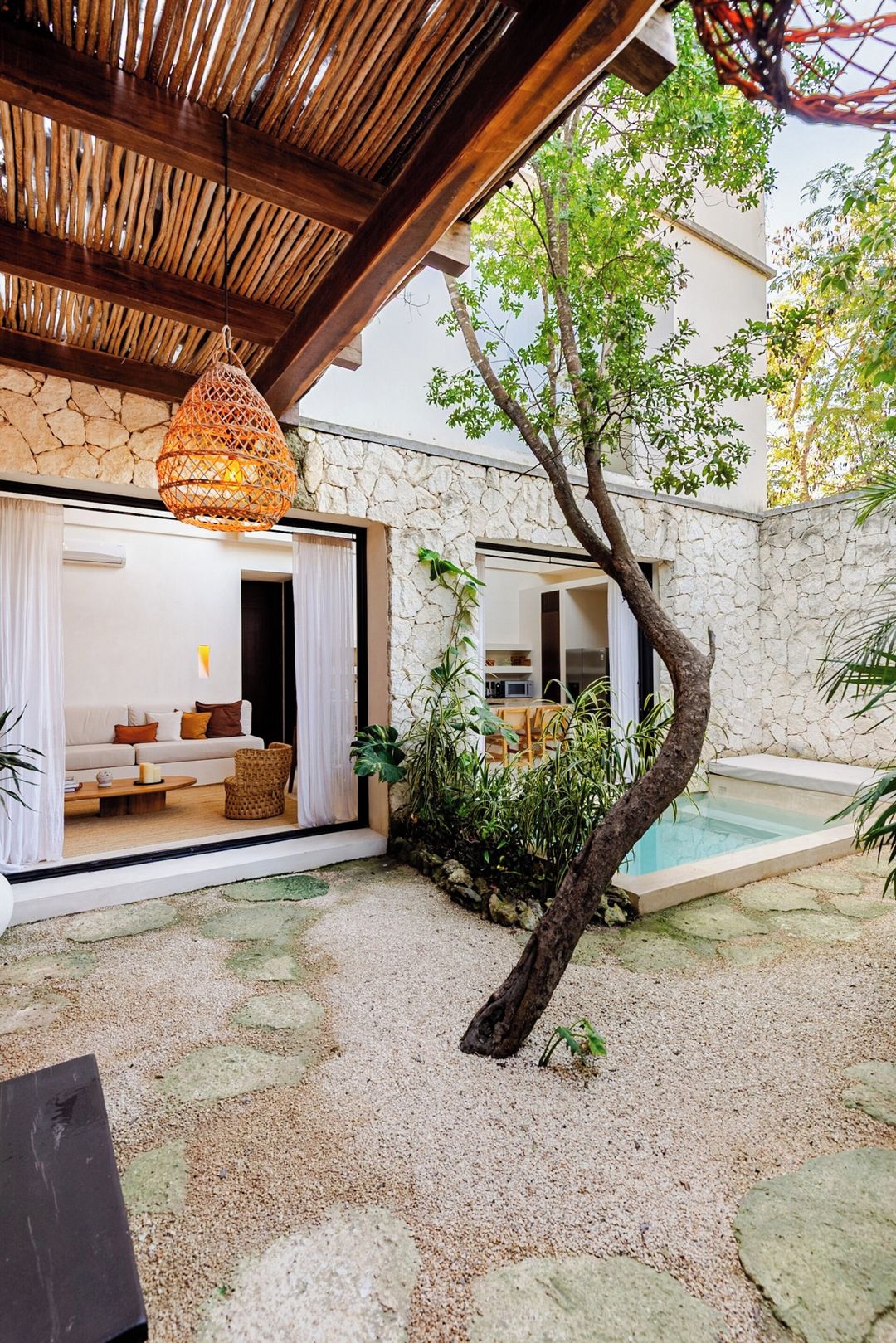 A modern outdoor living area with a stone wall, a tree, a pool, and a hanging light fixture.