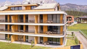 Un hotel de varios pisos con un letrero que dice 'Kitzbühel Suites' y un paisaje montañoso de fondo.