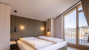 Un dormitorio con una cama, dos lámparas de noche, un ventanal con vistas y suelo de madera.