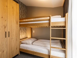 A bunk bed with a wooden frame and white bedding, a wardrobe with a wooden finish, and a patterned curtain. - Apartment in Fugen With Swimming Pool (Fuegen)