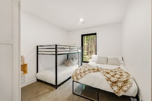Quarto com cama de solteiro, uma cama individual e janela com vista para árvores.