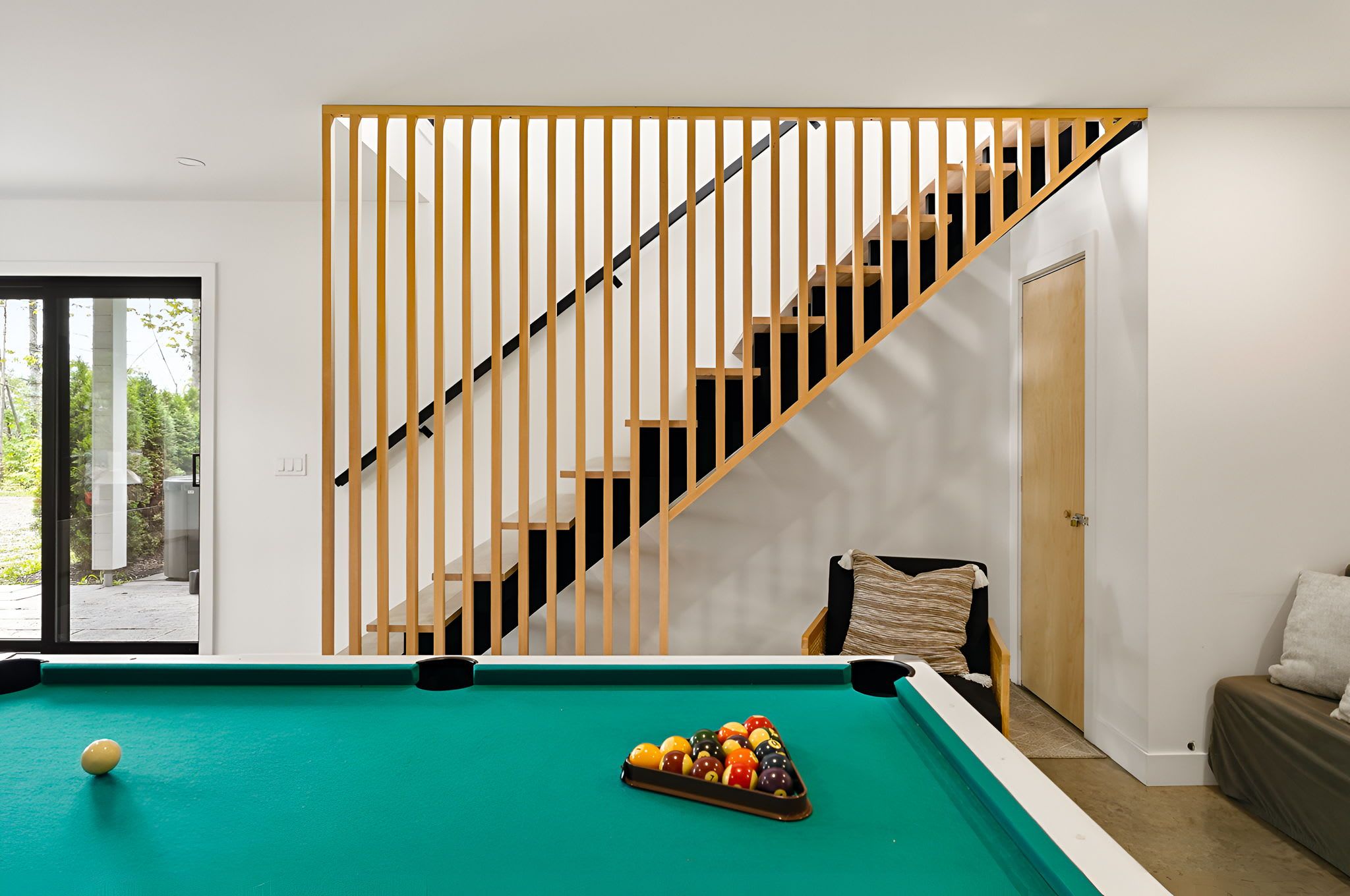 Una habitación con mesa de billar, una silla, un sofá y una escalera.