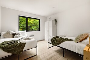 A modern bedroom with two beds, a wardrobe, and a window with a view of greenery. - Spa, Nature & Comfort | Le Repère Alpin (Adstock)