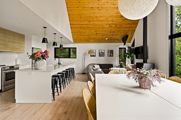 Une cuisine moderne dotée d’un îlot central, un coin repas avec une table blanche et un espace de vie comprenant un canapé et un téléviseur.