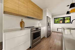 A modern kitchen with white cabinetry, stainless steel appliances, and a wooden ceiling. - Spa, Nature & Comfort | Le Repère Alpin (Adstock)
