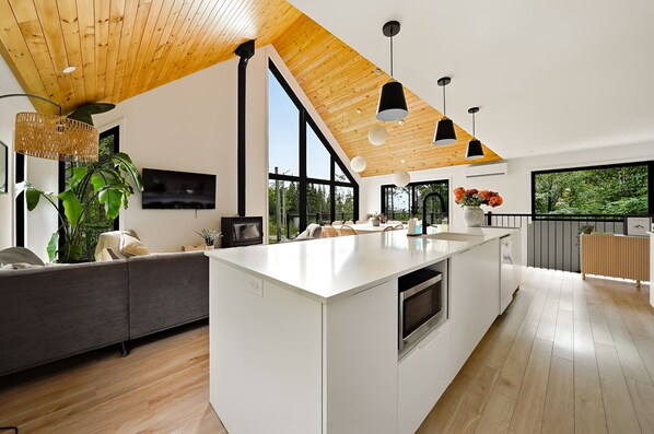 A modern kitchen with a large island, wooden ceiling, and large windows.
