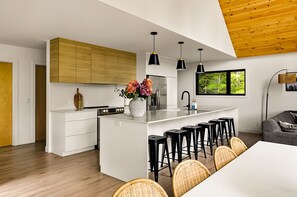 A modern kitchen with a central island, wooden cabinets, and a dining area with bar stools. - Spa, Nature & Comfort | Le Repère Alpin (Adstock)