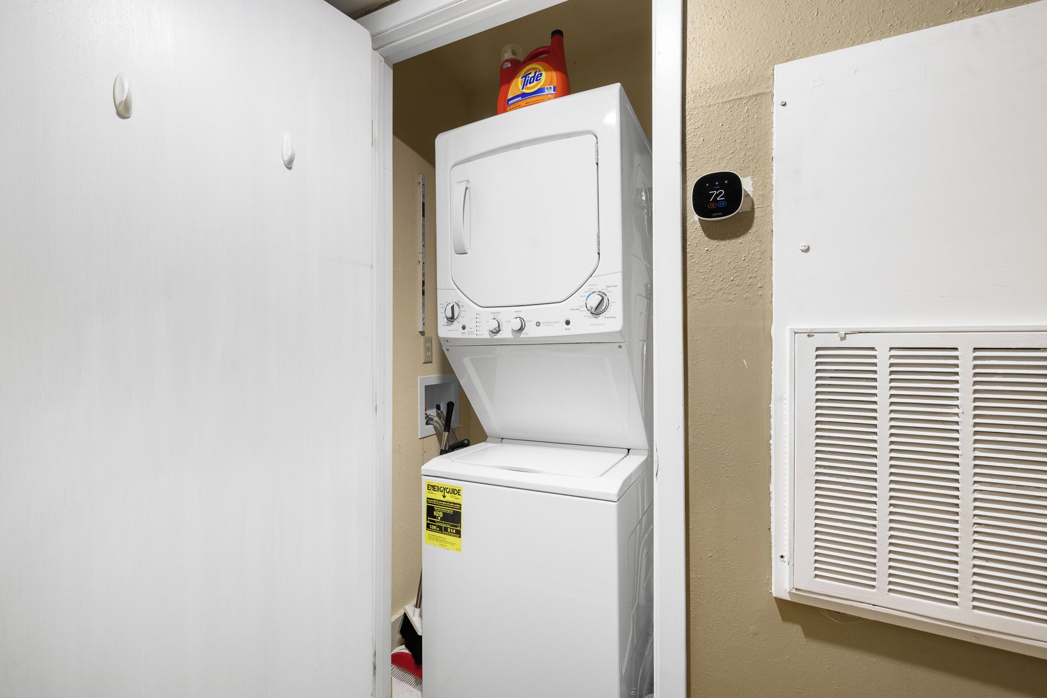 A laundry room with a front-loading washer and dryer, a Tide detergent bottle on the dryer, and a thermostat on the wall.