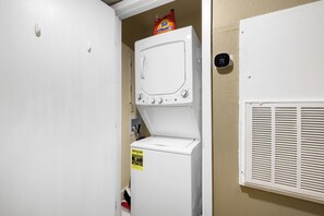A laundry room with a front-loading washer and dryer, a Tide detergent bottle on the dryer, and a thermostat on the wall. - Cozy 2BR/2BA near TAMU w/ Pool & Washer (College Station)