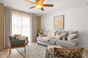 Un salon avec un canapé, un fauteuil et un ventilateur de plafond.