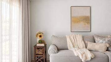 A living room with a grey sofa, a white throw blanket, and a small wooden side table with a vase of flowers.