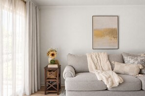 A living room with a grey sofa, a white throw blanket, and a small wooden side table with a vase of flowers. - Cozy 2BR/2BA near TAMU w/ Pool & Washer (College Station)