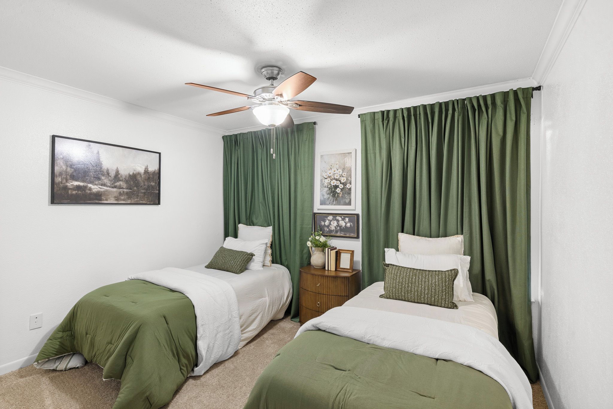 A bedroom with two beds, green curtains, a ceiling fan, and a painting on the wall.