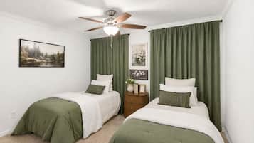 A bedroom with two beds, a ceiling fan, and green curtains.