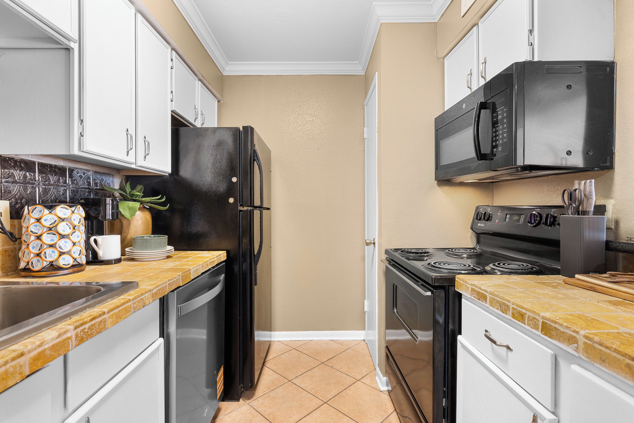 A compact kitchen with a black refrigerator, a microwave, a stove, and a sink.