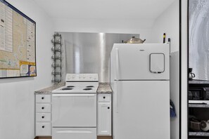 A compact kitchen with a white stove, a refrigerator, and a wall-mounted wine rack.