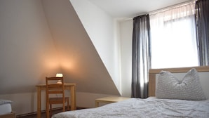A bedroom with a bed, a chair, a small table, and a window with curtains. - Holiday Home Neuhausen – Attic Apartment / 2 Bedrooms / Wi-Fi (Neuhausen)