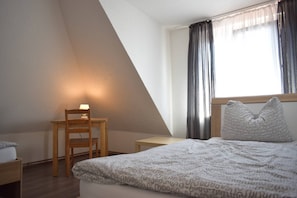 Un dormitorio con cama, una silla, una mesita y una ventana con cortinas.