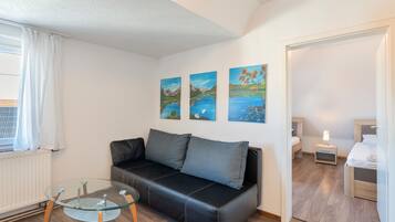 Ein modernes Wohnzimmer mit einem schwarzen Ledersofa, einem Glastisch und einem Gemälde mit einer Seelandschaft an der Wand.