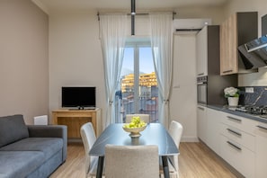 Une cuisine moderne avec un coin repas, un téléviseur à écran plat et une vue sur les immeubles par la fenêtre.