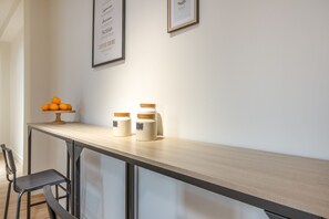 Un coin cuisine avec un plan de travail en bois, deux bocaux avec leurs couvercles, un saladier rempli d’oranges et une chaise.