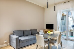 Un salon moderne avec un canapé gris, une table à manger avec des chaises, un téléviseur à écran plat et une grande fenêtre avec des rideaux.
