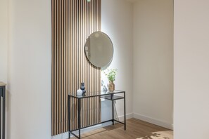 A room with a wooden slat wall, a round mirror, a glass table with a vase, and a potted plant. - Apartment 'Room 002' with Sea View, Wi-Fi, and Air Conditioning (Catania)