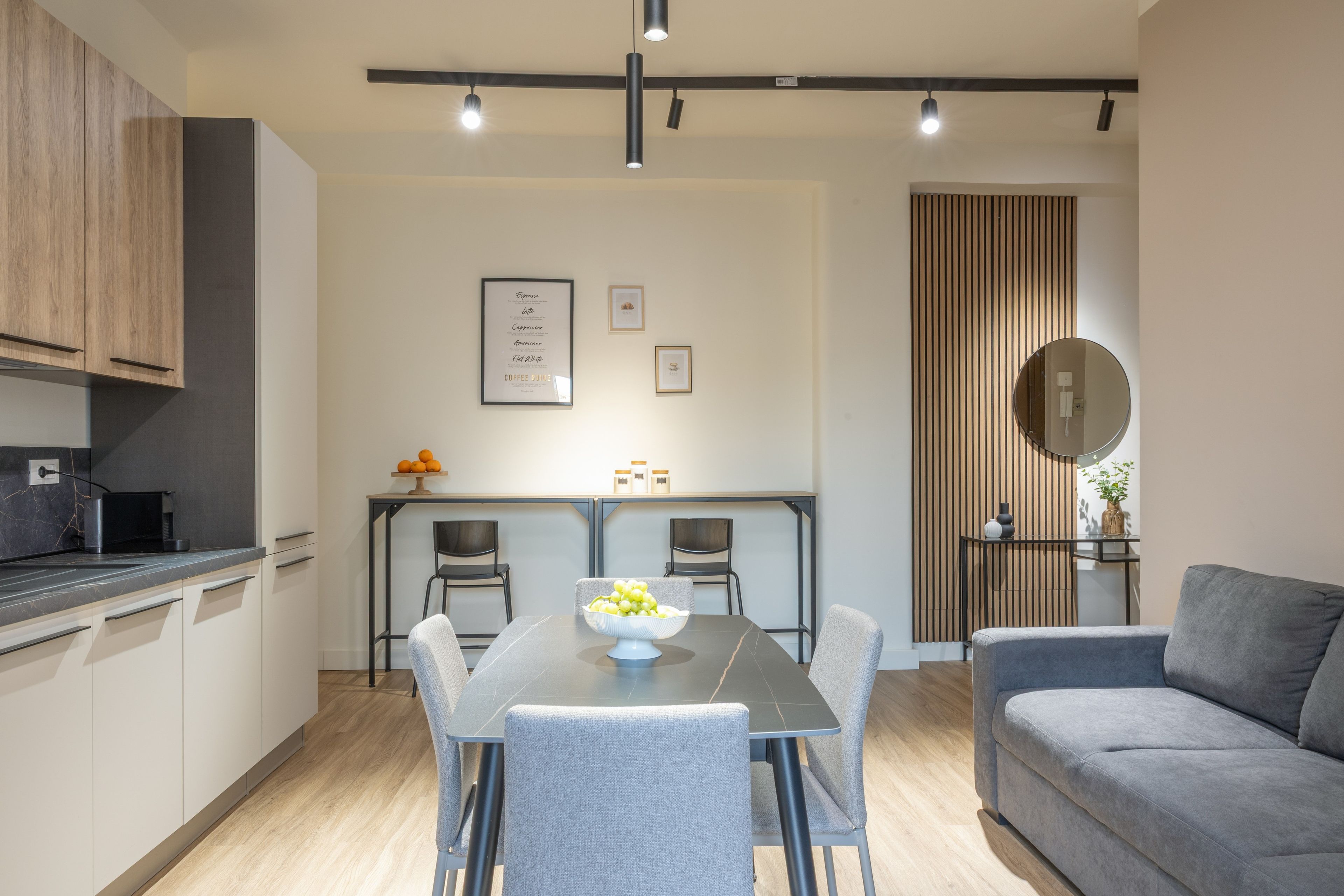 A modern kitchen with a dining area, a grey sofa, and a wooden accent wall.