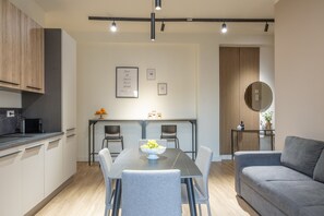 A modern kitchen with a dining area, a grey sofa, and a wooden accent wall. - Apartment 'Room 002' with Sea View, Wi-Fi, and Air Conditioning (Catania)