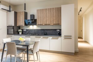 A modern kitchen with a dining area, featuring a built-in oven, a sink, and a black marble countertop. - Salamon House - Room 003 (Catania)