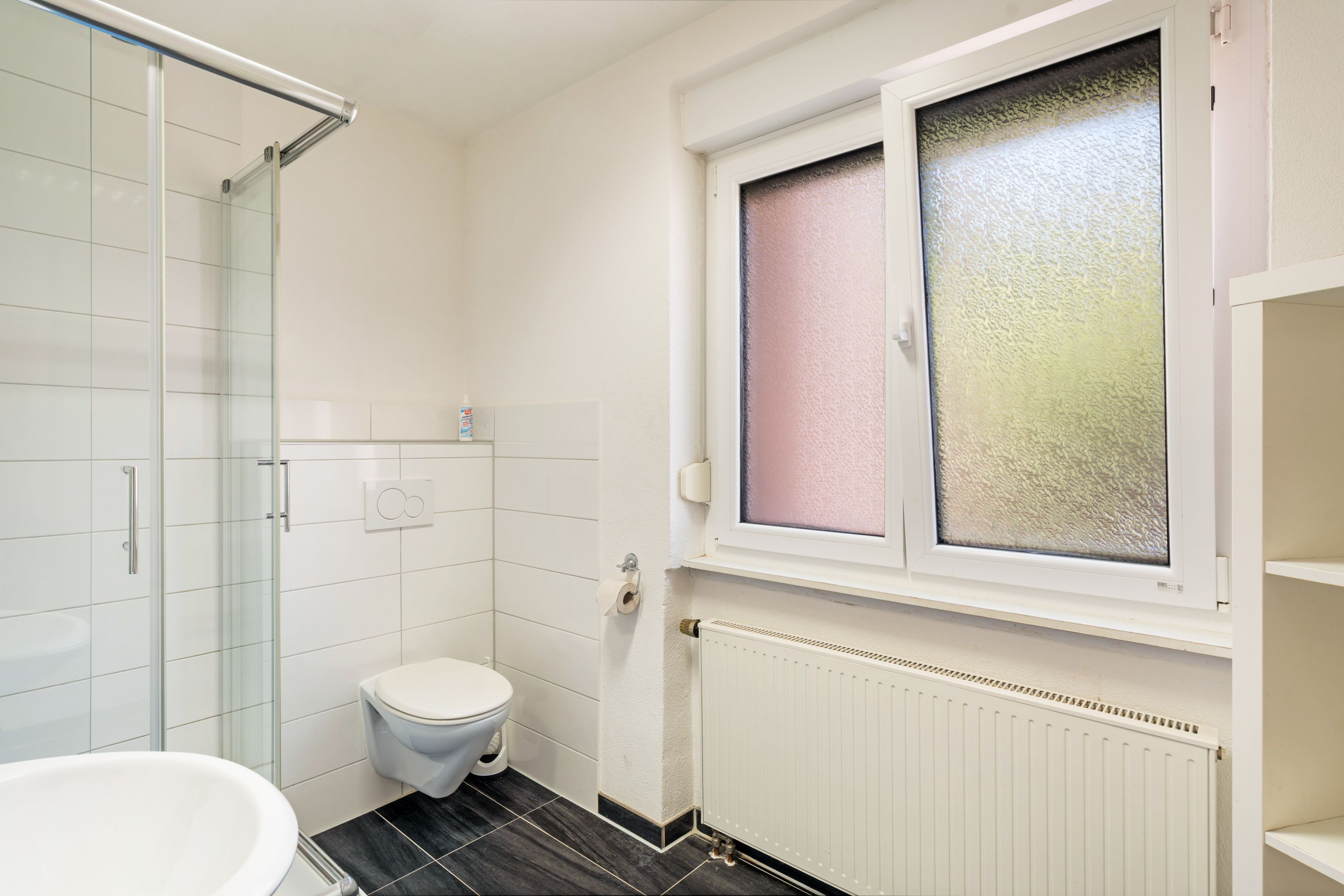 A bathroom with a toilet, a shower, and a window with frosted glass.
