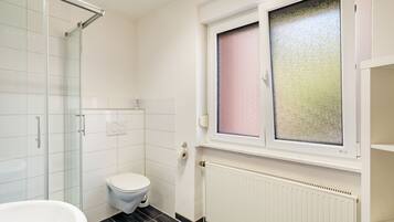 A bathroom with a toilet, a shower, and a window with frosted glass.