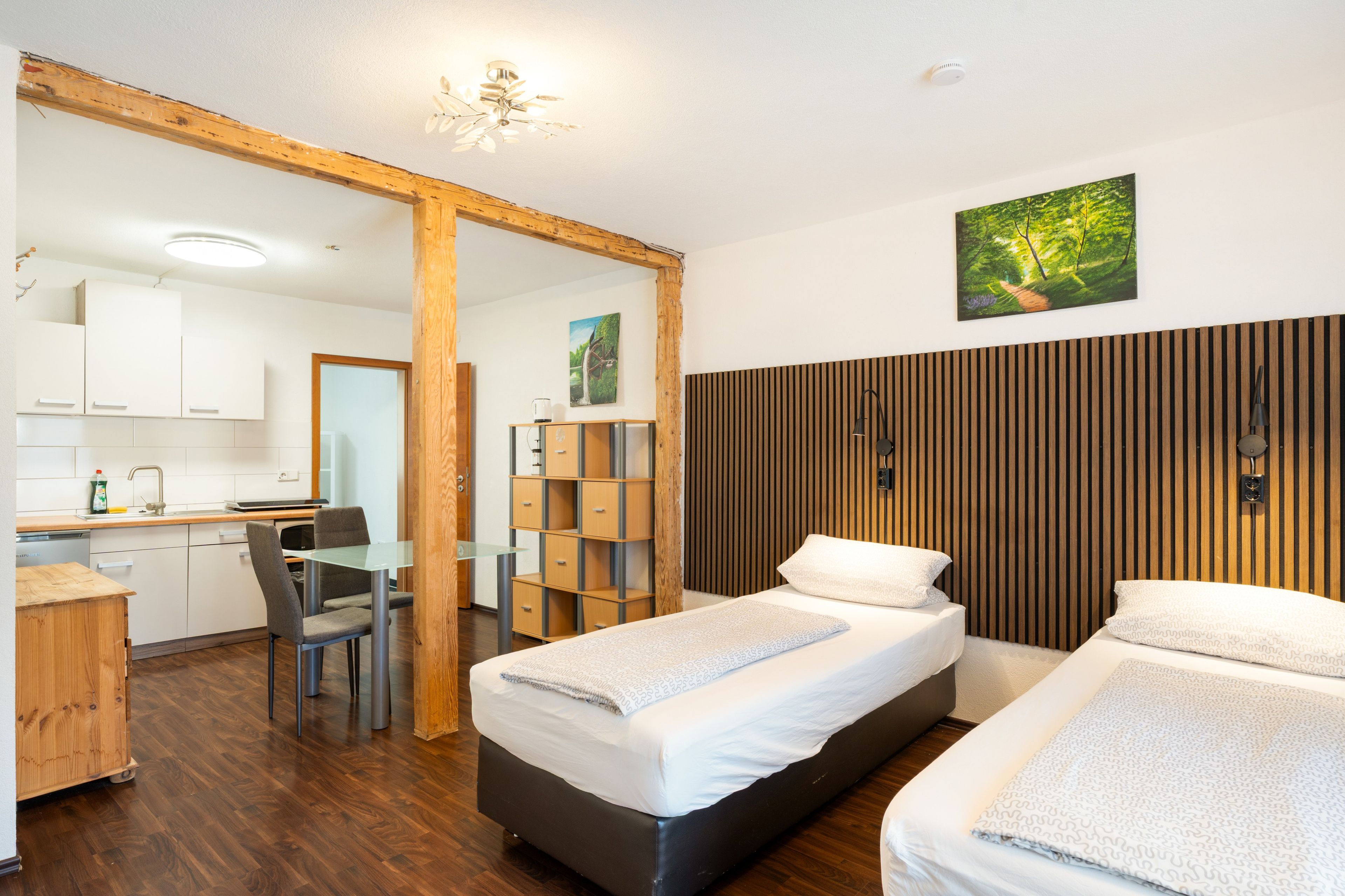 Ein modernes Schlafzimmer mit zwei Betten, einem Holzkopfstück, einem Schreibtisch und einer Küchenzeile.
